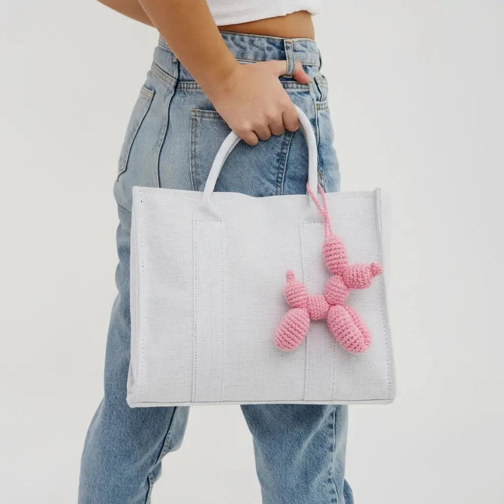 White tote bag with pink crocheted charm, held by someone in blue jeans