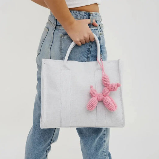 White tote bag with pink crocheted charm, held by someone in blue jeans