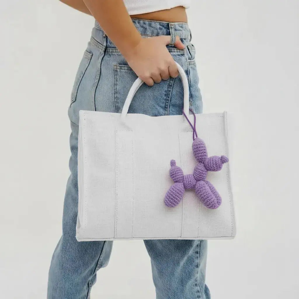 White tote bag with purple crocheted dog charm, held by someone in blue jeans