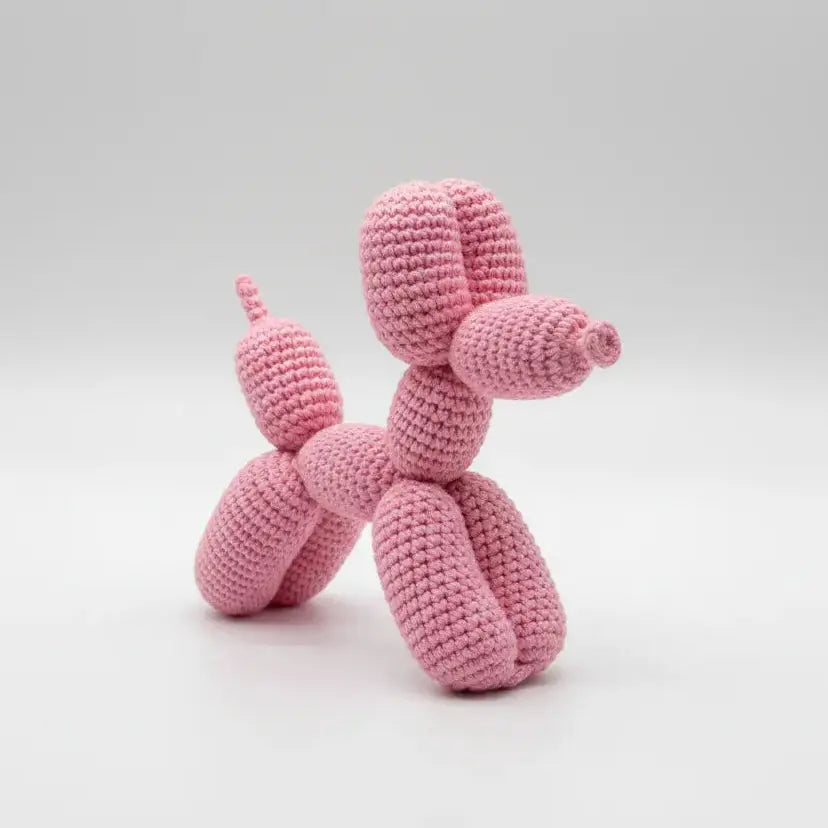 Pink crocheted balloon dog sculpture on a light gray background
