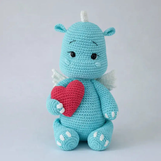 Crocheted blue creature with a red heart on a light gray background