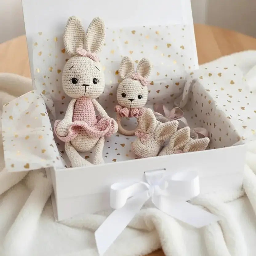 Two crocheted bunny dolls in pink and cream, nestled in a gift box with golden dots