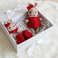 Two crocheted bunny dolls in red outfits nestled in a white gift box with shredded paper