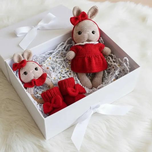 Two crocheted bunny dolls in red outfits nestled in a white gift box with shredded paper