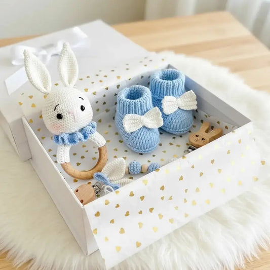 Handmade knitted blue baby booties and white bunny rattle in a heart-patterned gift box