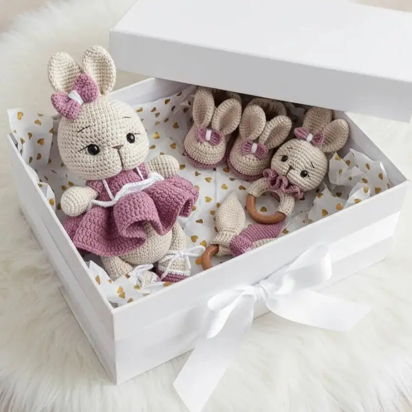 Crocheted bunny dolls in pink and cream inside a gift box with white bow