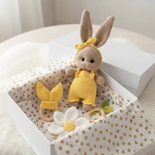 Crocheted bunny in yellow outfit sitting in heart-patterned gift box with daisy