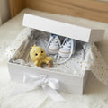 Crocheted yellow chick and blue baby booties nestled in a gift box with white ribbon