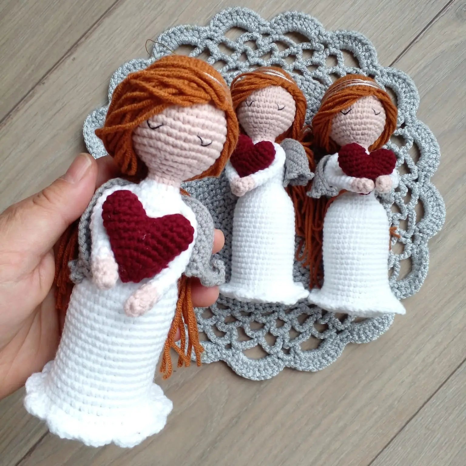 Three crocheted angels with red hearts on white gowns against a gray lace doily backdrop