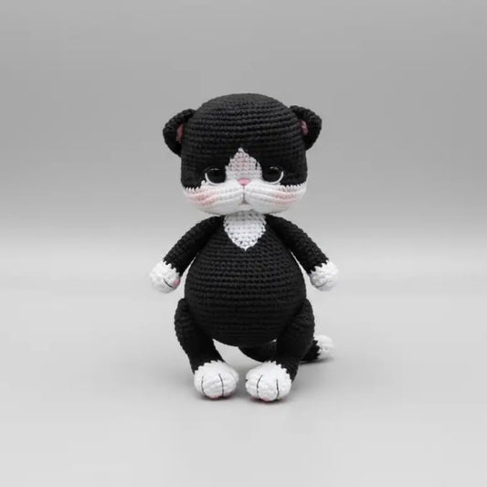 Crocheted black and white cat plush toy sitting on a plain background