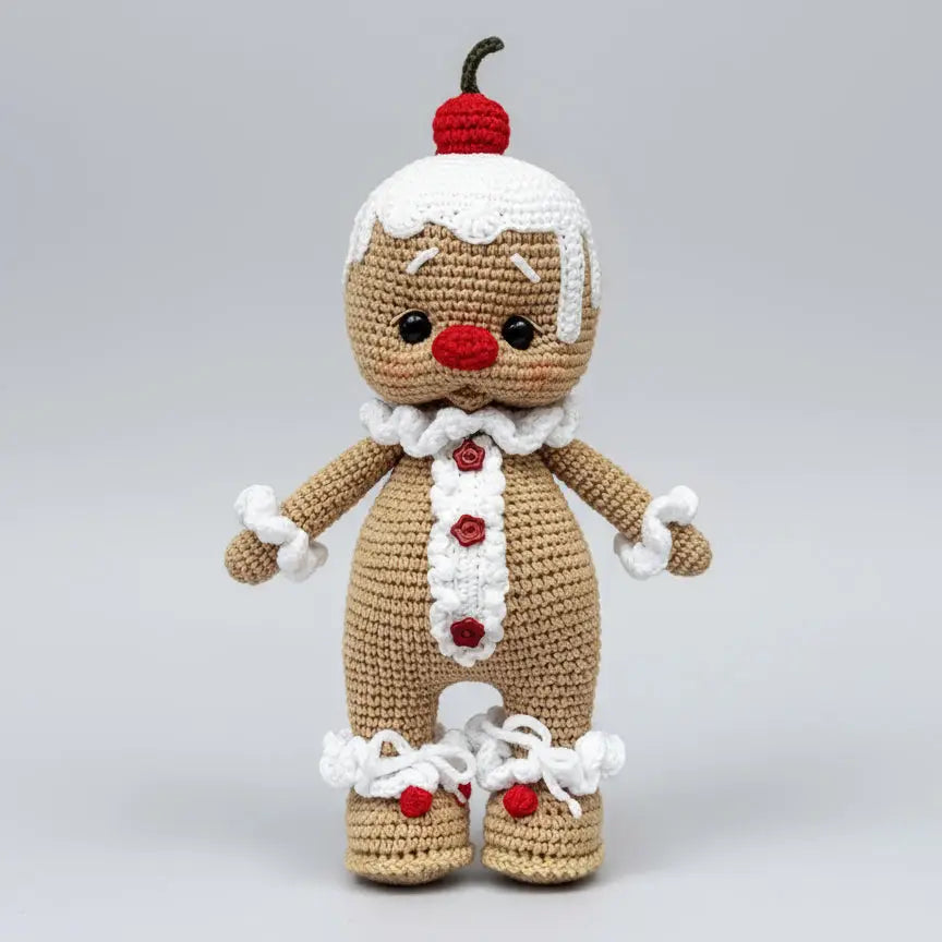 Crocheted gingerbread person with red cherry on head, white trim, and red buttons