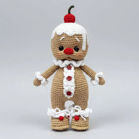 Crocheted gingerbread person with red cherry on head, white trim, and red buttons