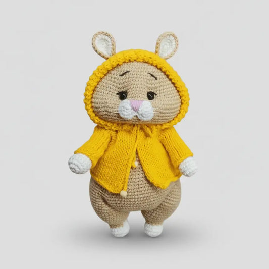 Crocheted bunny in bright yellow raincoat, sitting on white background