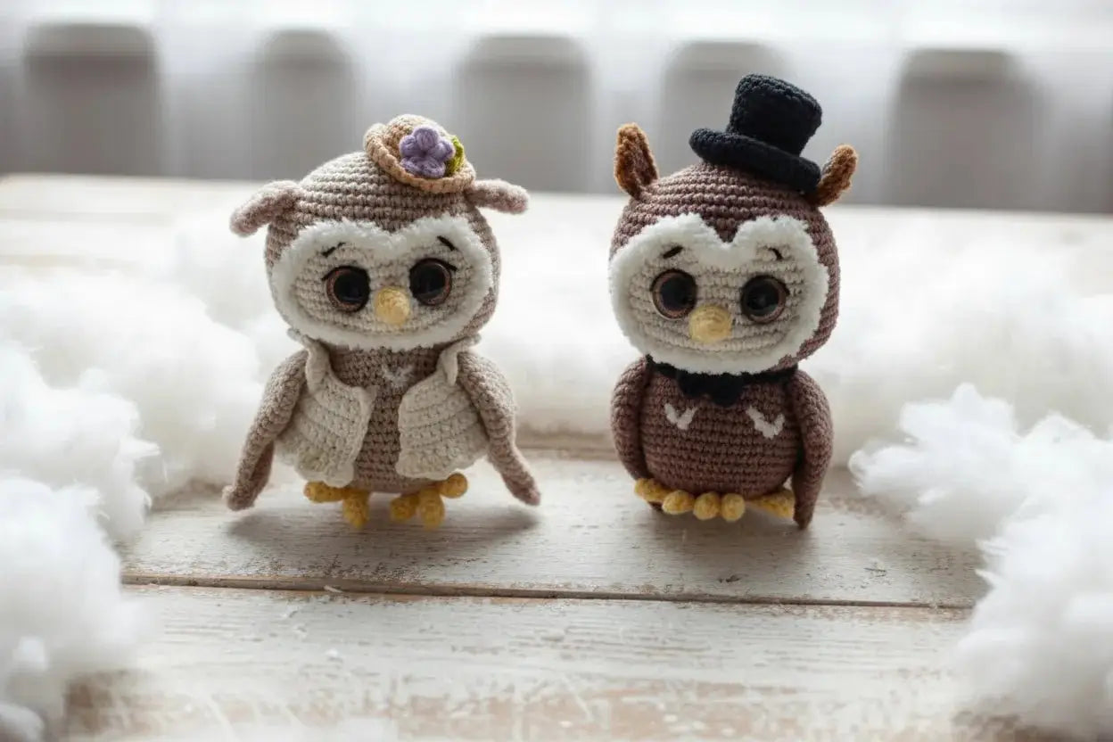 Two crocheted owls in wedding attire, bride and groom, sitting on wooden surface