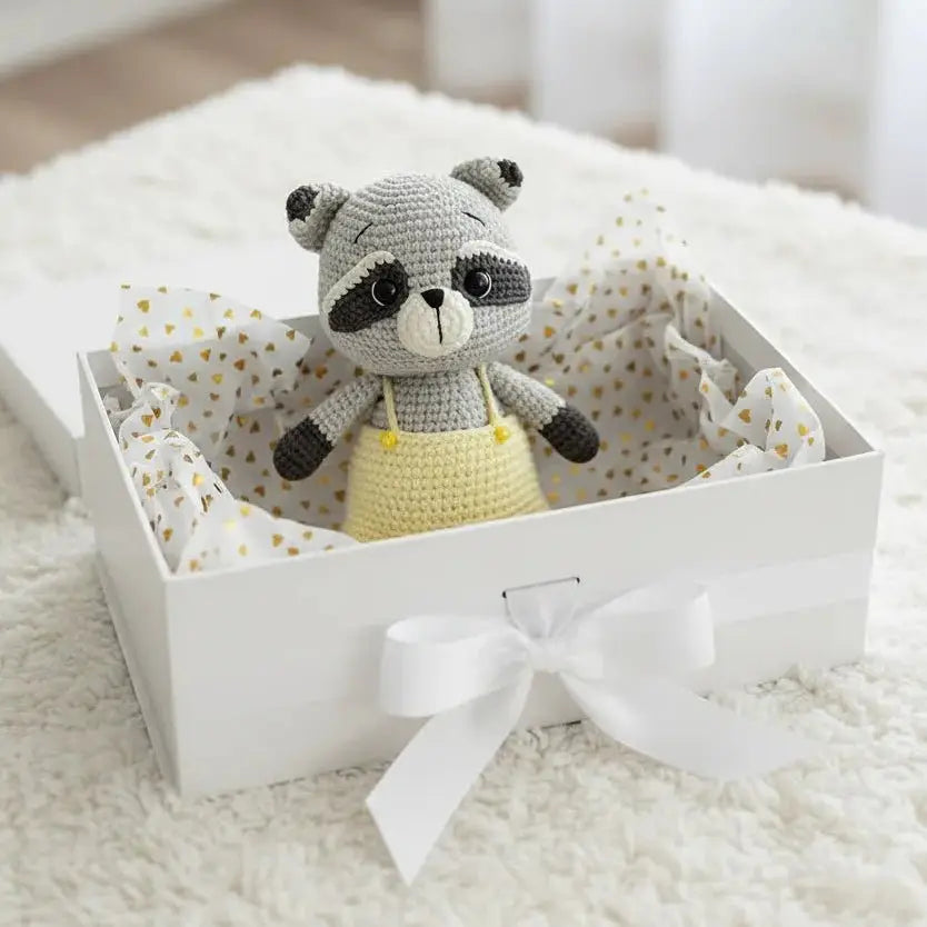 Crocheted raccoon stuffed animal in a white gift box with polka dot tissue paper