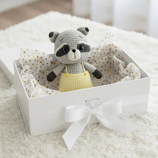 Crocheted raccoon stuffed animal in a white gift box with polka dot tissue paper