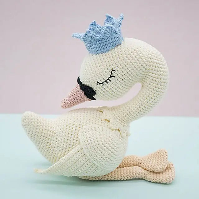 Crocheted white swan with blue crown, sitting gracefully on pastel background