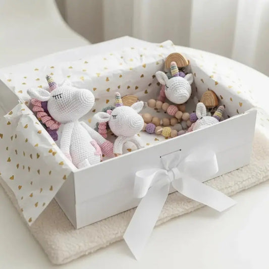 Crocheted unicorns and wooden toys nestled in a white gift box with gold hearts and bow