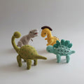 Four crocheted dinosaurs in different colors and species, standing together on a white surface