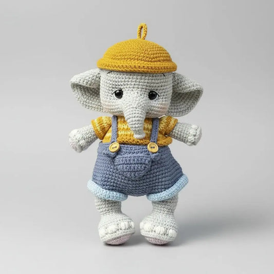 Crocheted elephant doll wearing yellow hat and blue overalls on gray background