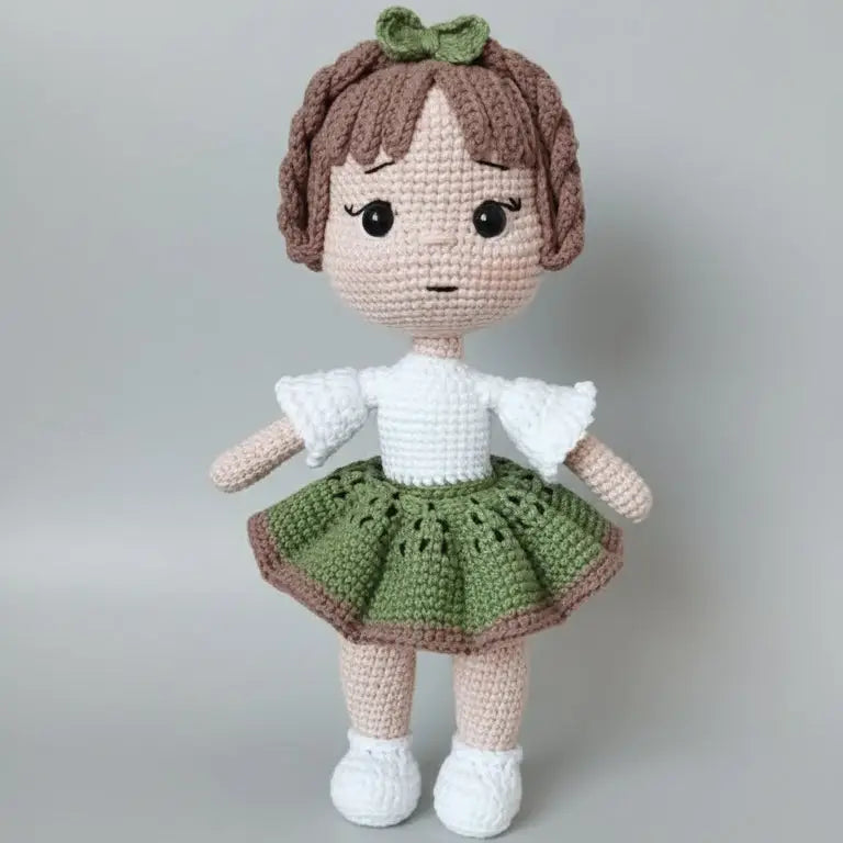 Crocheted doll with brown hair, green skirt, and white shirt standing against gray background