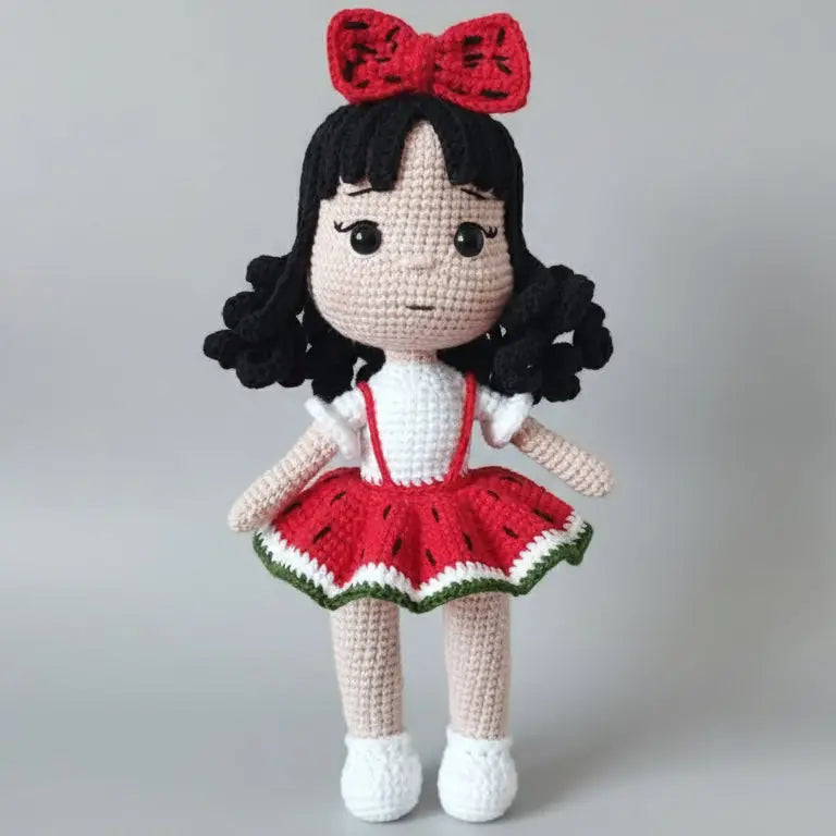 Crocheted doll with black curly hair, red bow, and watermelon-themed dress, standing cute