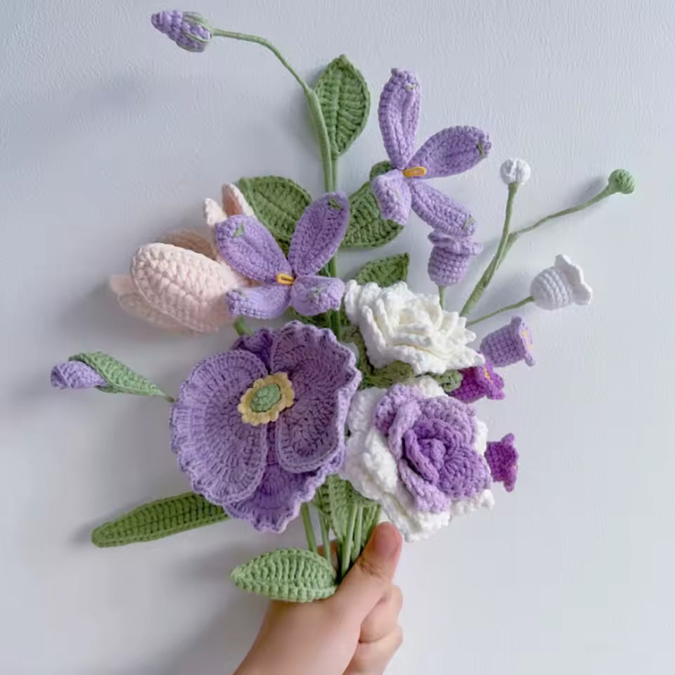 Crocheted bouquet of purple and white flowers with green leaves, held by a hand