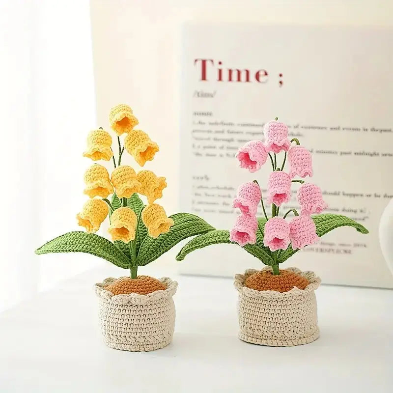Crocheted yellow and pink bell-shaped flowers in ceramic pots against dictionary page