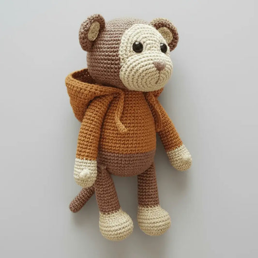 Crocheted teddy bear in brown and cream, wearing an orange scarf