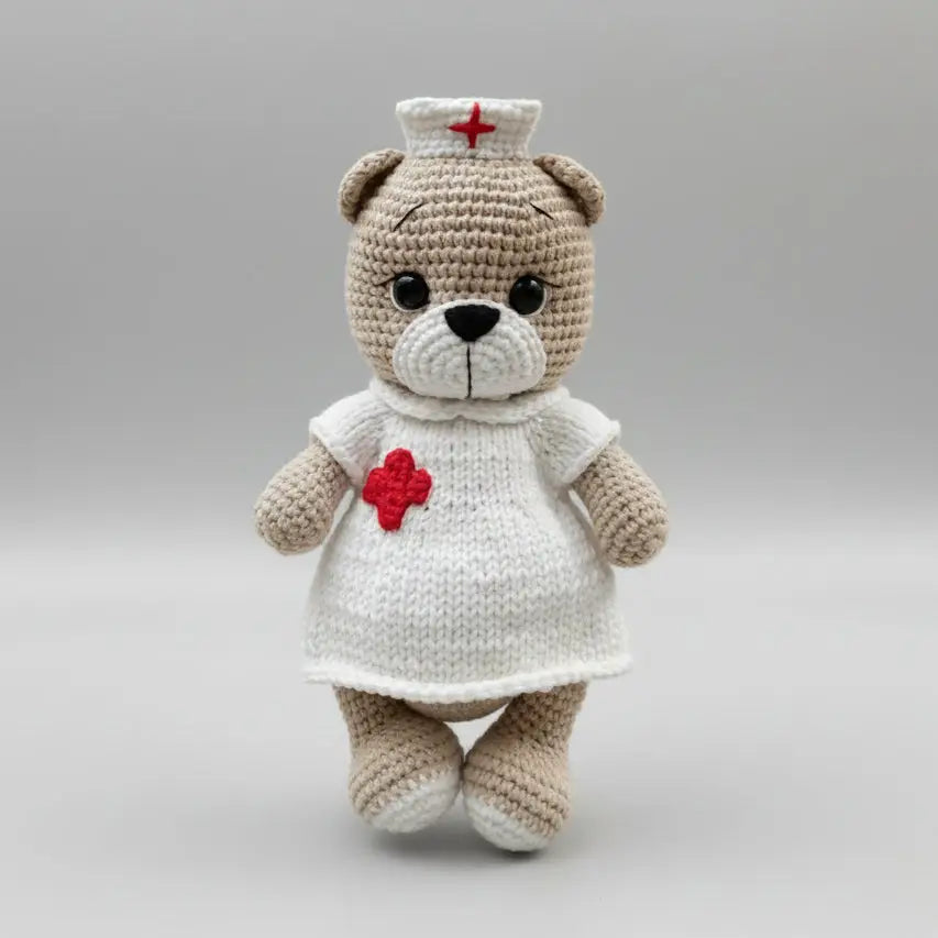 Crocheted teddy bear in white nurse uniform with red cross hat and badge
