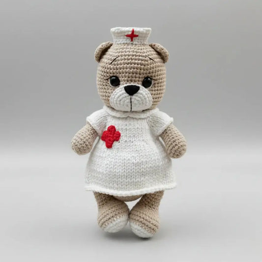 Crocheted teddy bear in white nurse uniform with red cross hat and badge