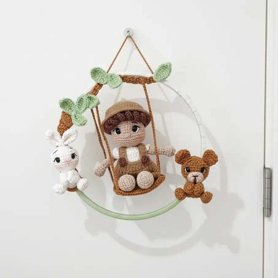 Crocheted doll on swing with bunny and teddy bear, hanging from leafy branch