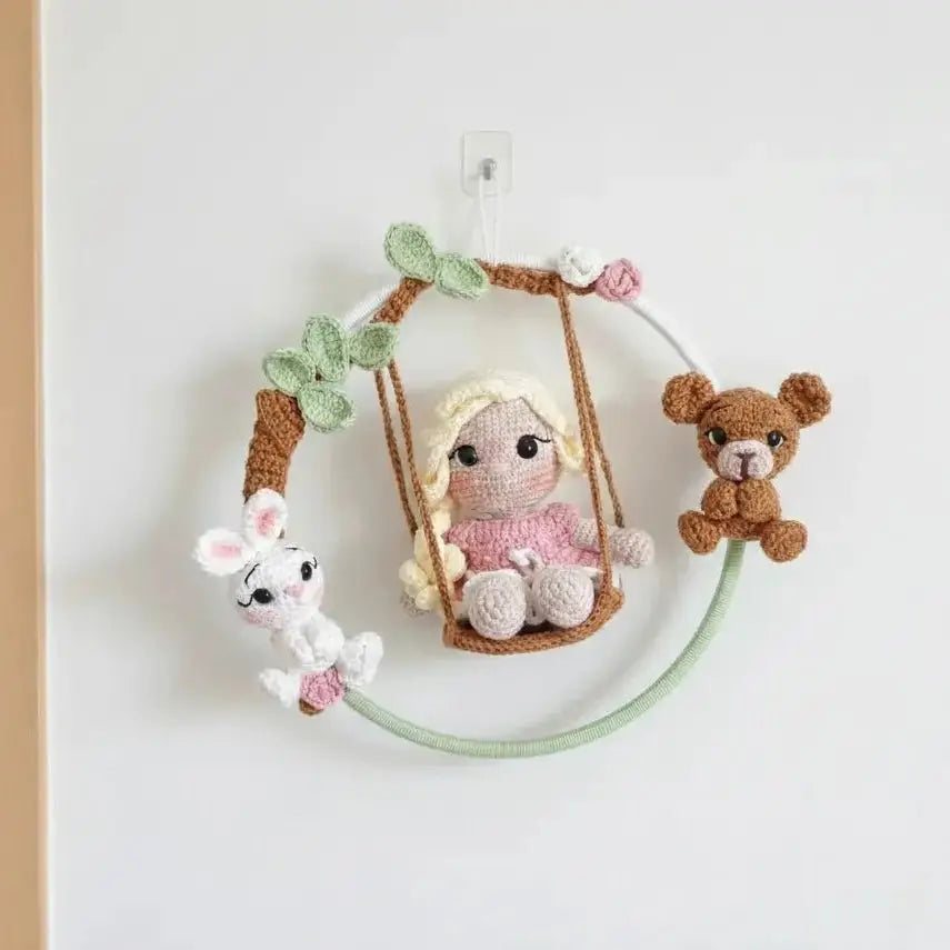 Crocheted doll on swing with bunny and teddy bear, surrounded by pastel leaves and flowers