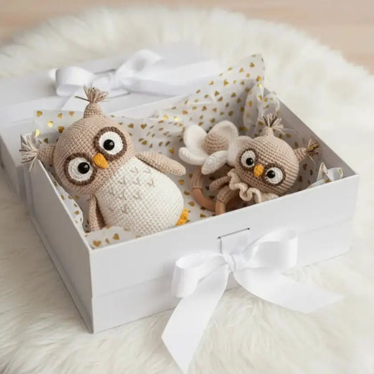Two crocheted owl toys nestled in a white gift box with gold-dotted lining and a white bow.