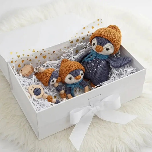 Crocheted penguin dolls in cozy winter outfits nestled in a gift box with white ribbon
