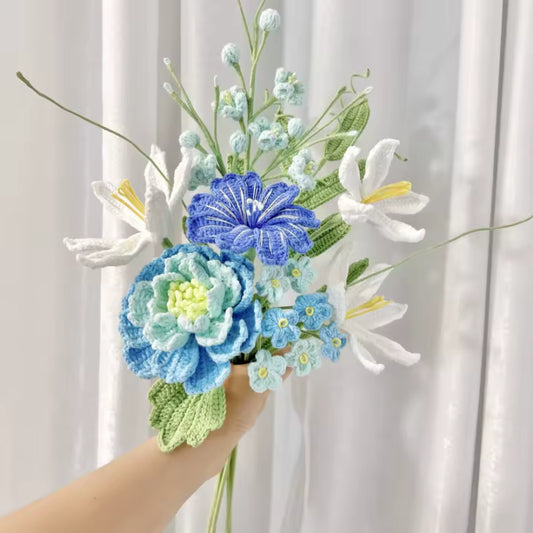 Hand holding crocheted bouquet of blue, white, and green flowers with delicate details