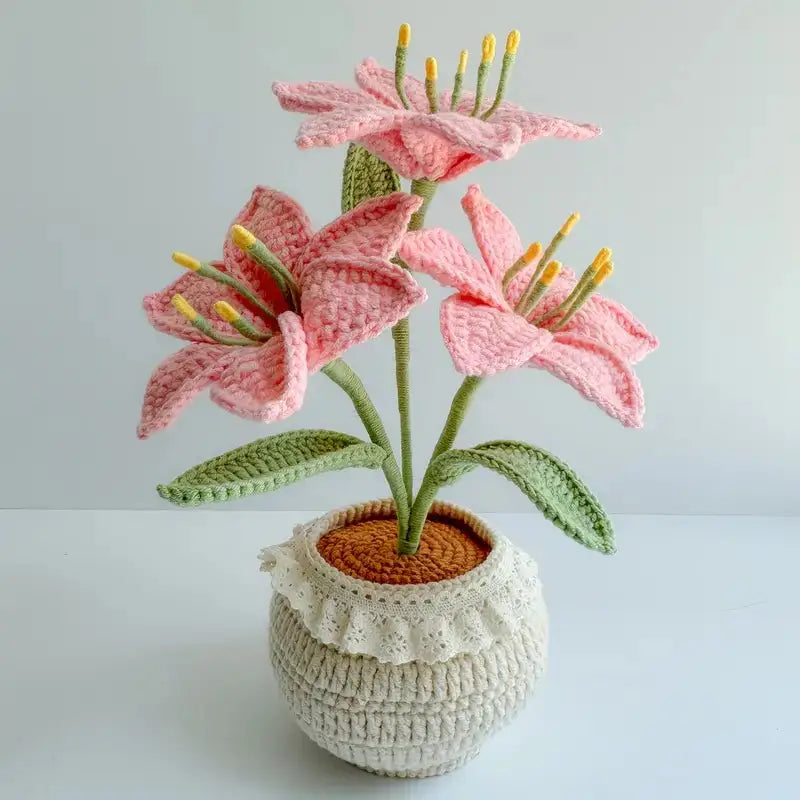 Crocheted pink lily flowers with green leaves in a textured white pot