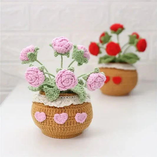 Crocheted pink roses in a heart-decorated clay pot with another pot of red flowers