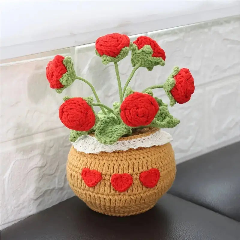 Crocheted red roses in a tan vase with heart decorations, sitting on a dark surface