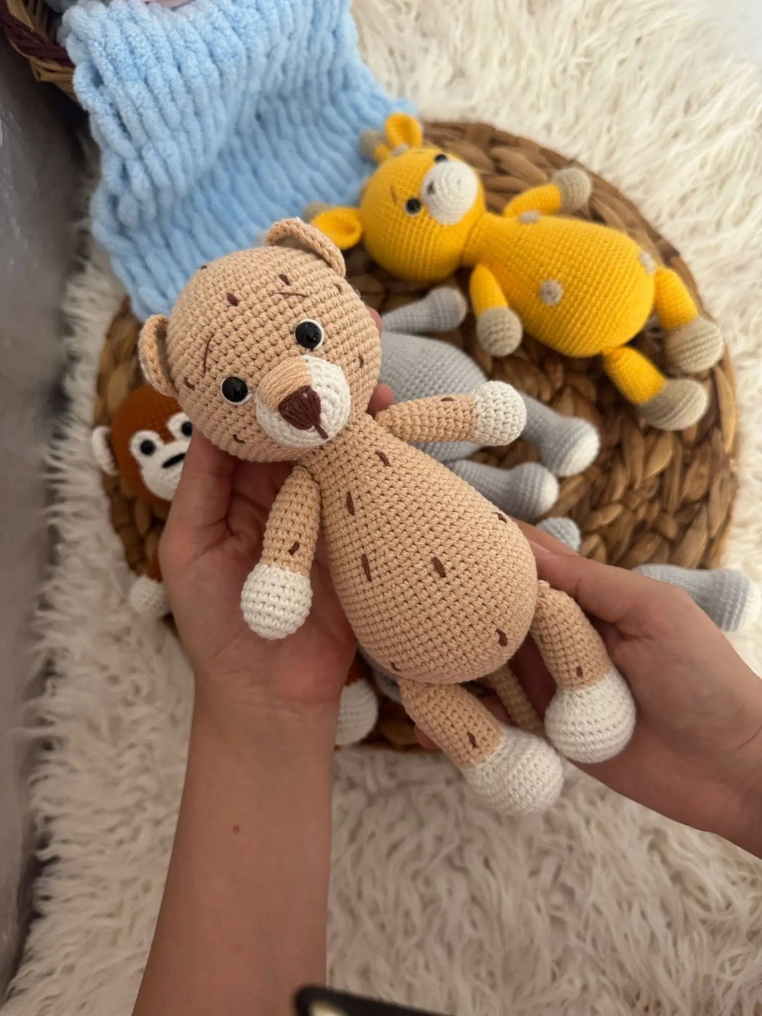 Crocheted tan teddy bear with white paws held in hand, yellow toy in background