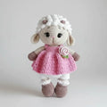 Crocheted lamb stuffed animal wearing pink dress with flower and white socks
