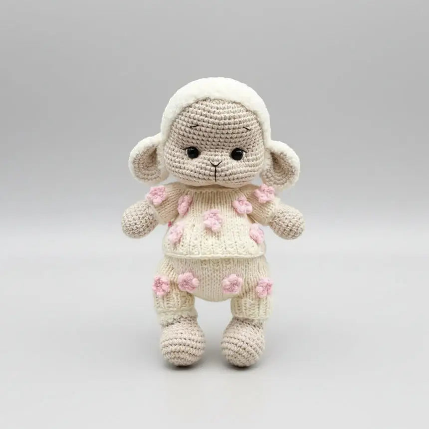 Crocheted lamb stuffed animal with pink flower details, standing on neutral background
