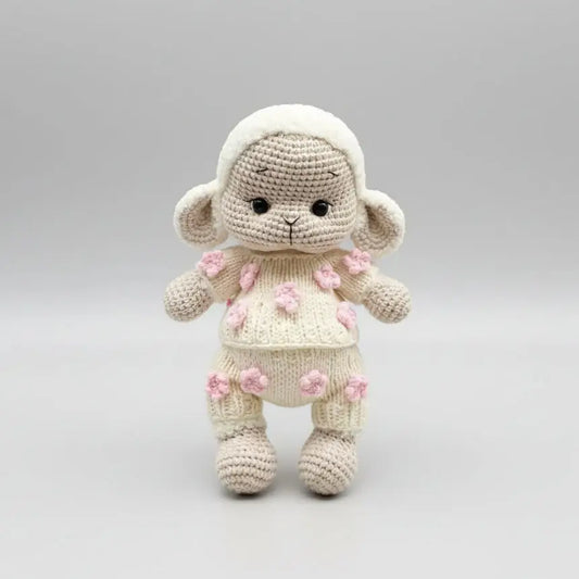 Crocheted lamb stuffed animal with pink flower details, standing on neutral background