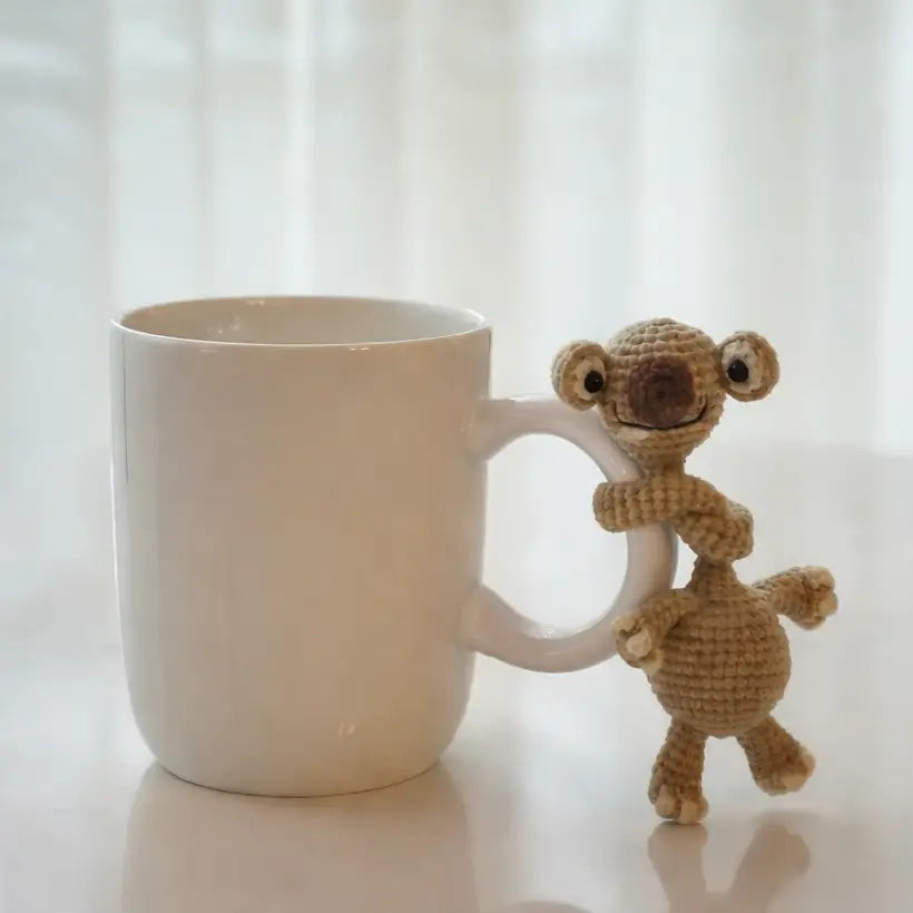 White mug with a small knitted monkey toy on a light surface with white curtains in the background