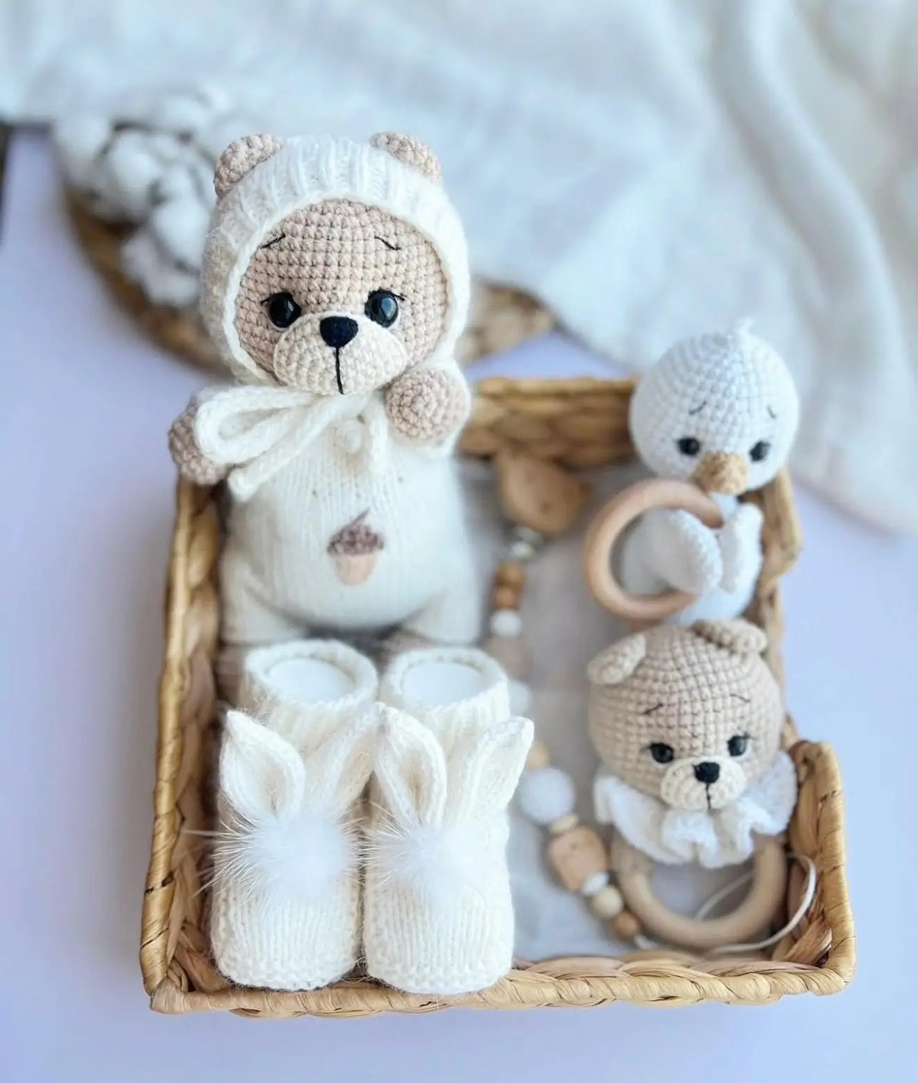 Crocheted teddy bear and bunny booties in woven basket with wooden teething ring