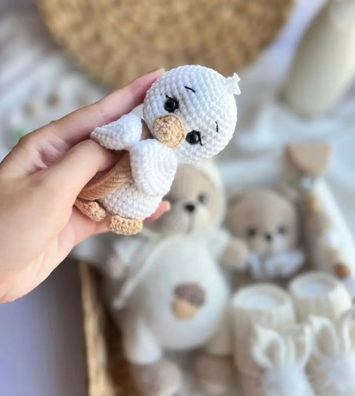 Crocheted white bird with beige beak, held in hand with blurred stuffed animals in background