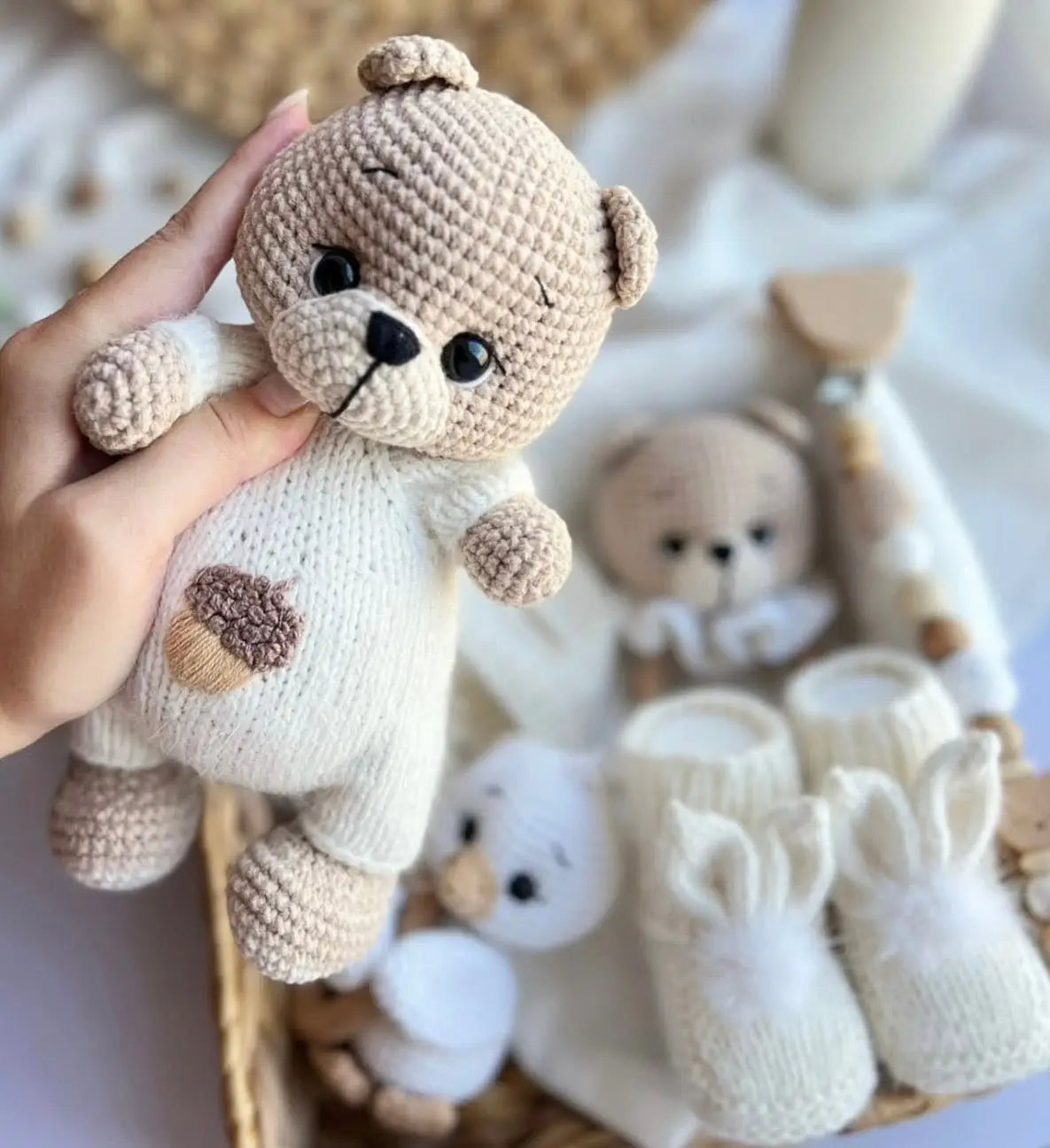 Crocheted teddy bear in cream and beige, held by a hand with soft toys in background.