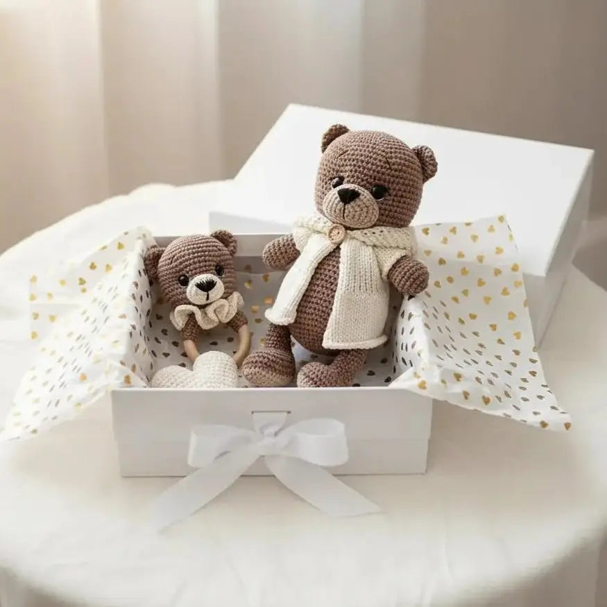 Two crocheted teddy bears in a white gift box with gold heart-patterned tissue paper and a white bow
