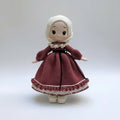 Crocheted doll in burgundy dress with white bonnet and lace collar, standing upright