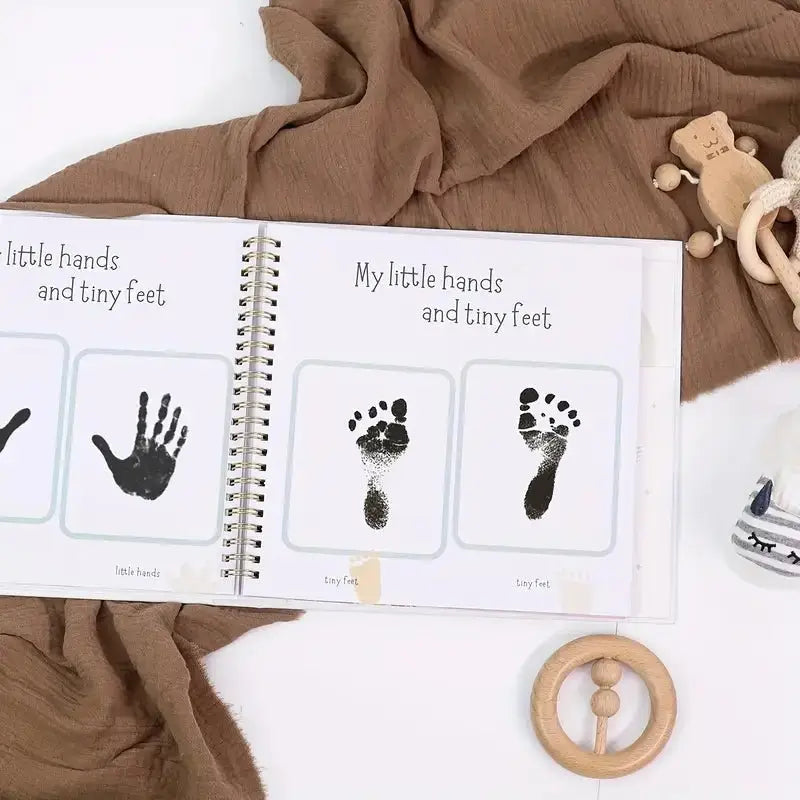 Baby milestone book with black ink hand and footprints on white pages, surrounded by wooden toys